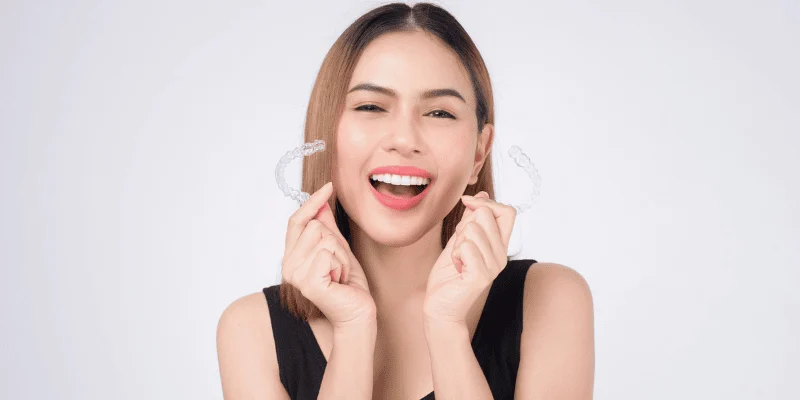 Smiling woman holding a clear aligner